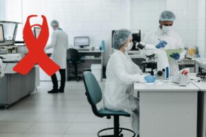 Investigadores en laboratorio analizando muestras con microscopio, símbolo de la cinta roja asociado a la investigación y concienciación sobre el cáncer.